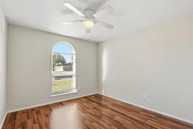 an empty room with wooden floor chandelier fan and windows