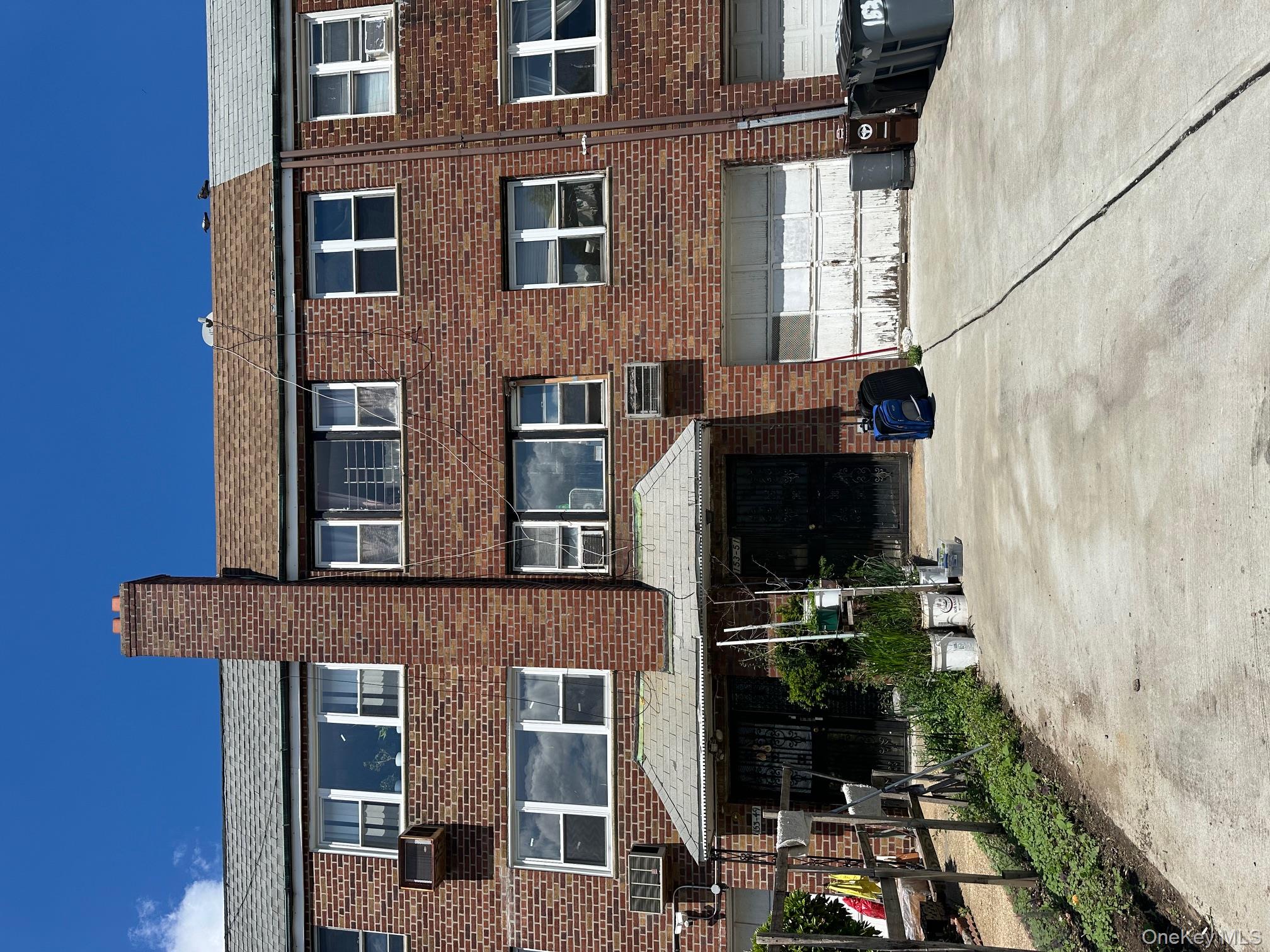 Rear view of house with brick siding, a chimney, driveway, and a shingled roof