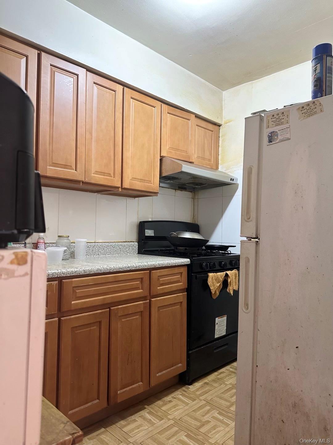 153-51 Horace Harding Expressway Queens, NY 11367 - Photo 3 of 11 Kitchen with freestanding refrigerator, black gas range oven, brown cabinets, refrigerator, and under cabinet range hood