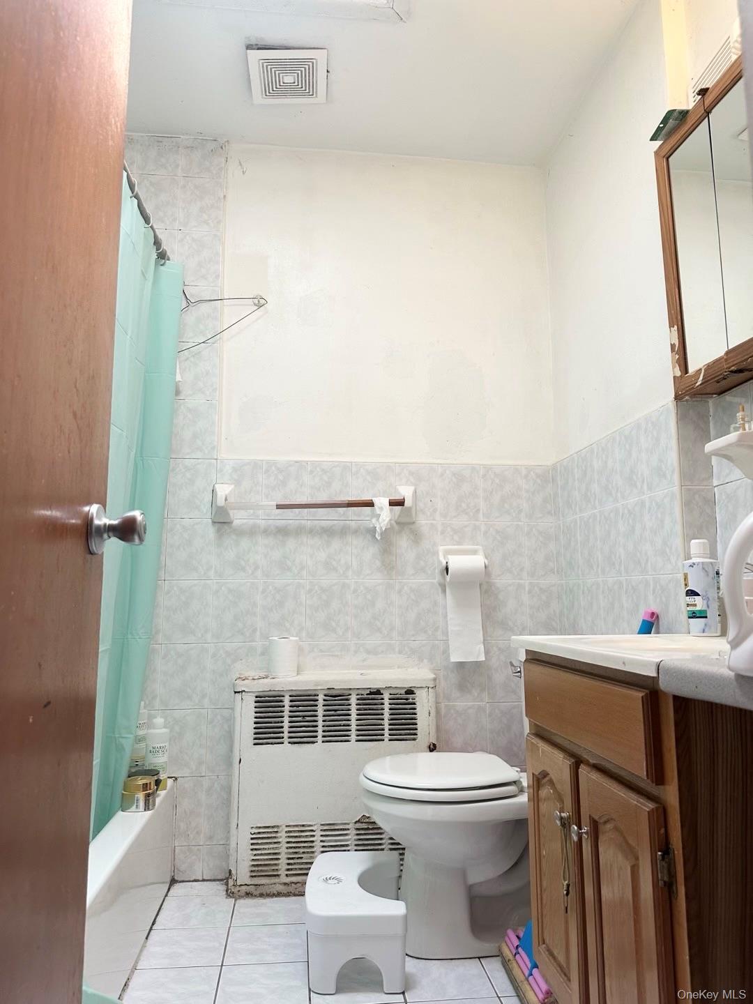 153-51 Horace Harding Expressway Queens, NY 11367 - Photo 4 of 11 Bathroom with light tile patterned floors, tile walls, shower / bath combination with curtain, vanity, and radiator heating unit