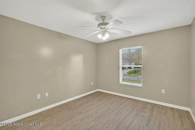 an empty room with wooden floor fan and windows
