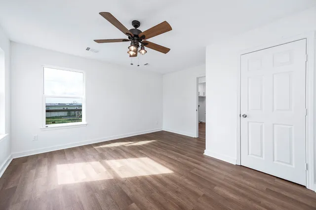 an empty room with wooden floor fan and windows