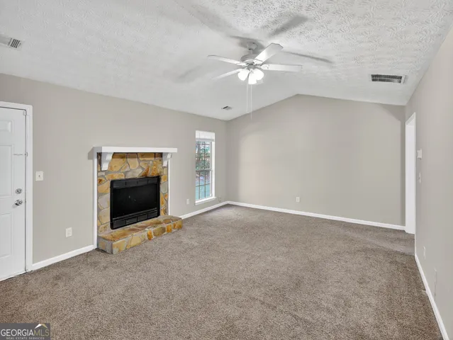 a view of an empty room with a fireplace and a ceiling fan