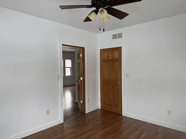 an empty room with wooden floor fan and windows