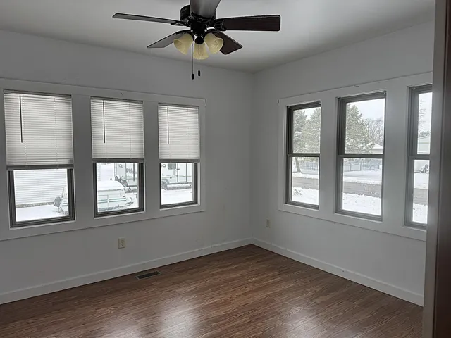 an empty room with wooden floor fan and windows