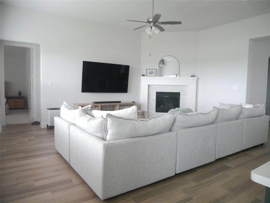 3201 Calvin Road McKinney, TX 75071 - Photo 2 of 11 Spacious living area featuring wood-finish flooring, a tiled fireplace with a mantel, and a ceiling fan