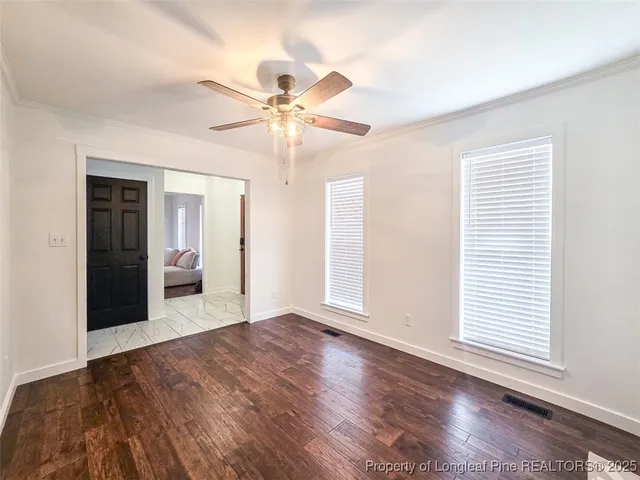 an empty room with wooden floor chandelier fan and windows