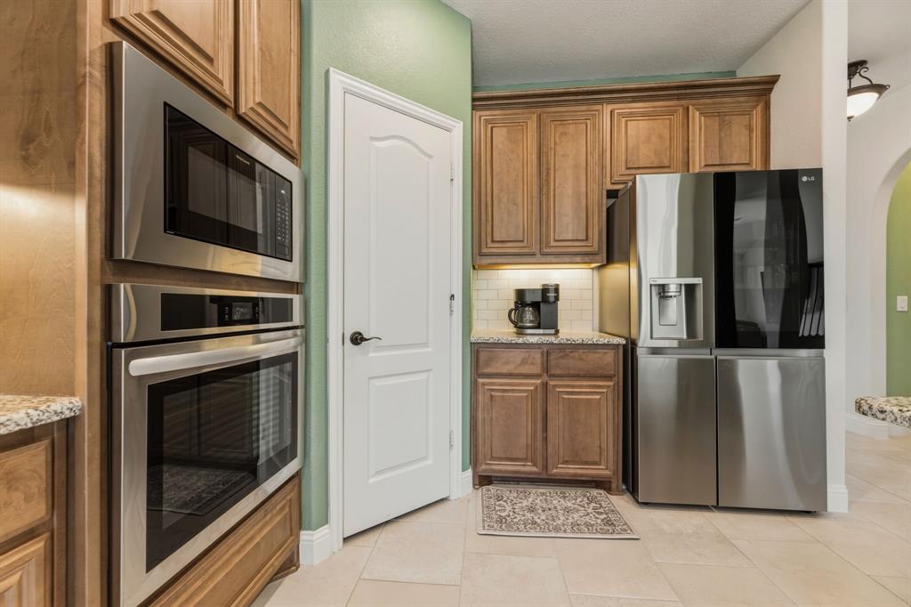 1030 Timber Ridge Drive Justin, TX 76247 - Photo 10 of 40 Kitchen with stainless steel appliances, wood finish cabinetry, light stone counters, and arched walkways