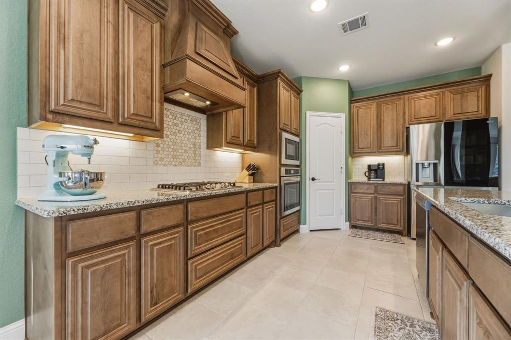 1030 Timber Ridge Drive Justin, TX 76247 - Photo 11 of 40 Kitchen featuring wood finish cabinetry, light stone counters, stainless steel appliances, light tile patterned flooring, and recessed lighting