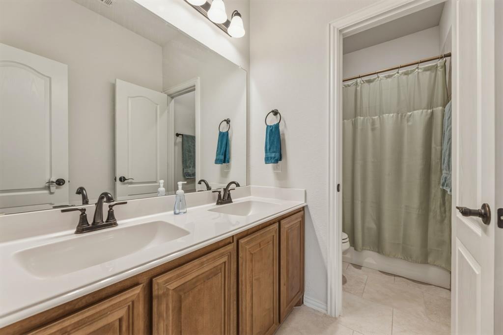 1030 Timber Ridge Drive Justin, TX 76247 - Photo 29 of 40 Full bathroom featuring double vanity, light tile patterned floors, and shower / tub combo with curtain