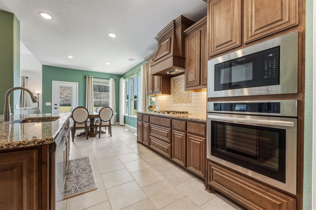 1030 Timber Ridge Drive Justin, TX 76247 - Photo 9 of 40 Kitchen with light stone countertops, stainless steel appliances, tasteful backsplash, light tile patterned flooring, and wood finish cabinets