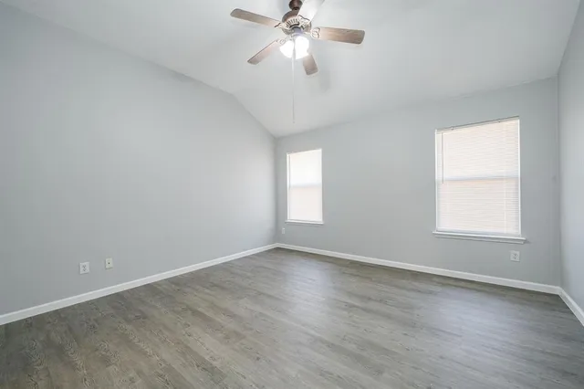 an empty room with wooden floor chandelier fan and windows