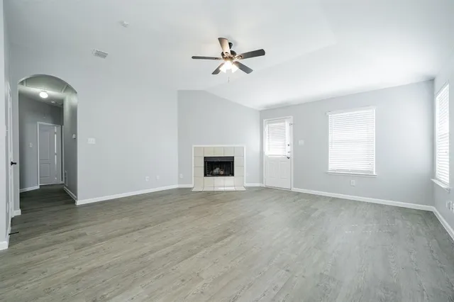 an empty room with wooden floor ceiling fan and windows