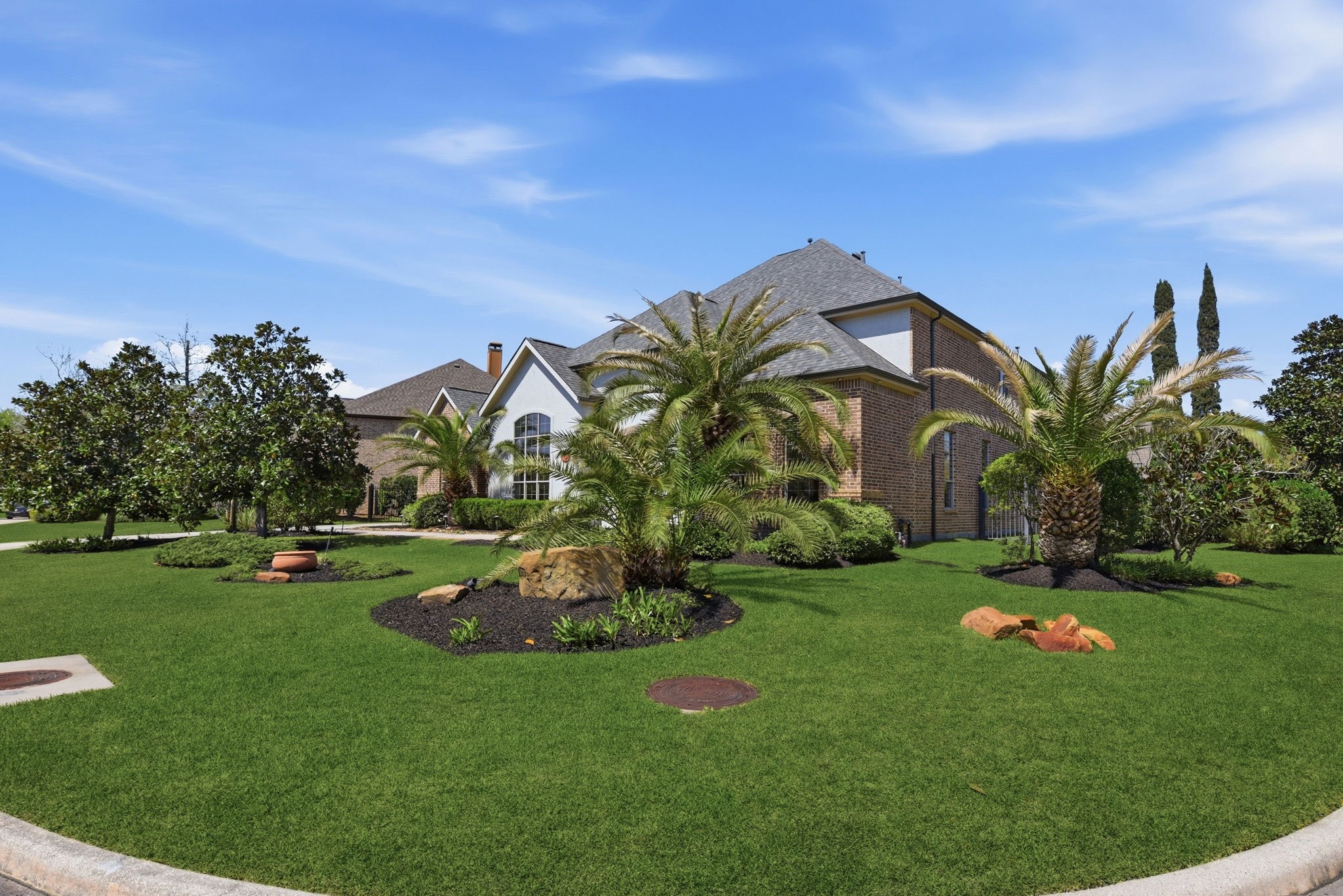 223 South Bauer Point Circle Spring, TX 77389 - Photo 5 of 50 This photo showcases a large brick home with a well-maintained lawn, palm trees, and landscaped greenery, set under a clear blue sky.