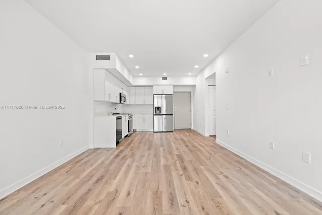 a view of kitchen and empty room with wooden floor