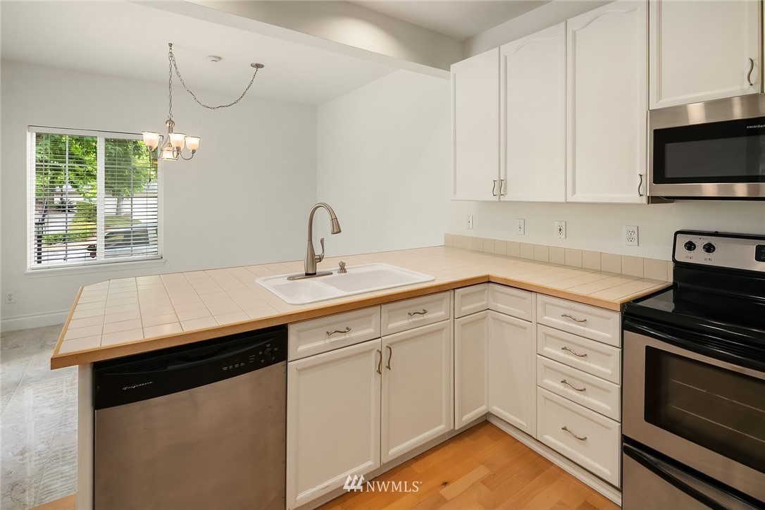 10909 Avondale Road Northeast, Unit F122 Redmond, WA 98052 - Photo 11 of 24 a kitchen with a sink dishwasher and white cabinets with wooden floor