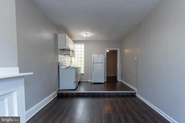 a view of an empty room with wooden floor and a kitchen