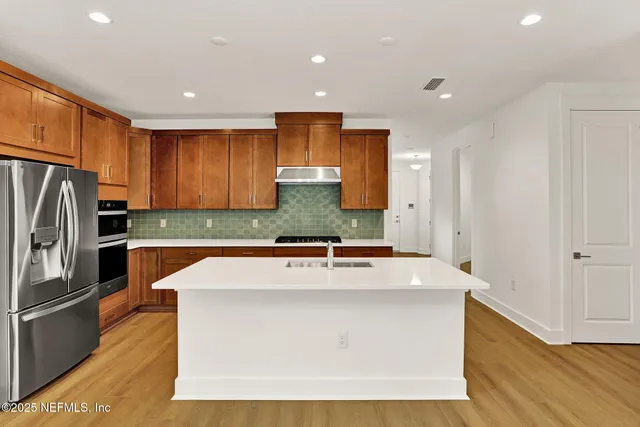 a view of a kitchen with stainless steel appliances granite countertop a stove a refrigerator a sink and dishwasher with wooden floor