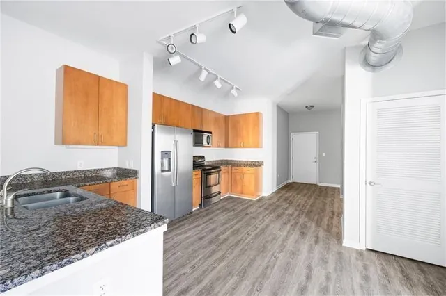 a kitchen with stainless steel appliances granite countertop a refrigerator a sink dishwasher a stove and white countertops with wooden floor