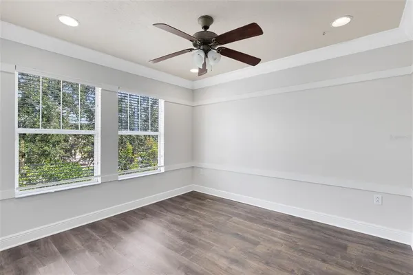 an empty room with wooden floor fan and windows