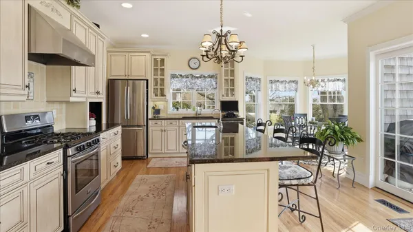a kitchen with stainless steel appliances kitchen island granite countertop a stove a refrigerator a sink a dining table and chairs with wooden floor