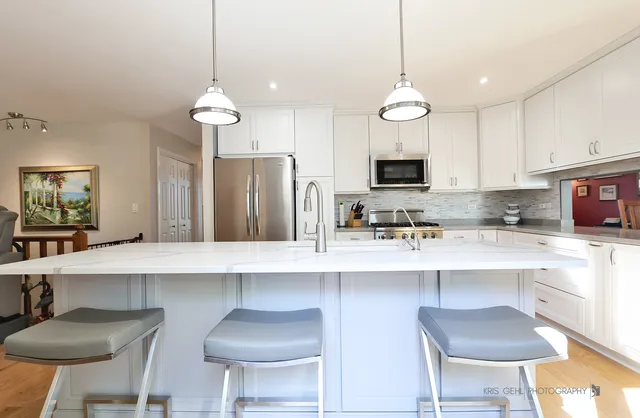 a kitchen with stainless steel appliances a stove a refrigerator and a dining table with white cabinets