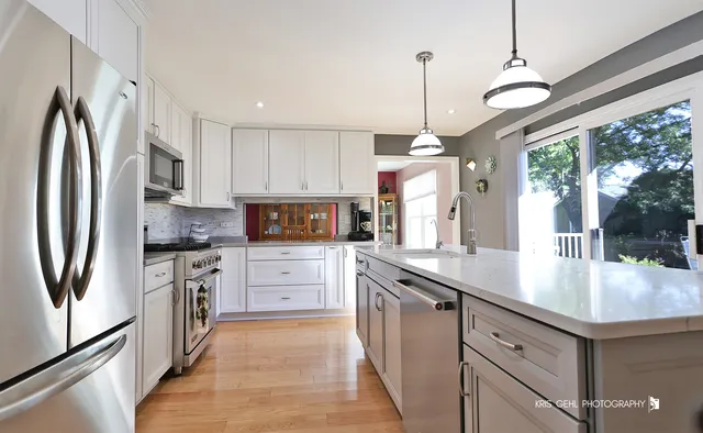 a kitchen with stainless steel appliances granite countertop a refrigerator a sink dishwasher a stove and white countertops with wooden floor