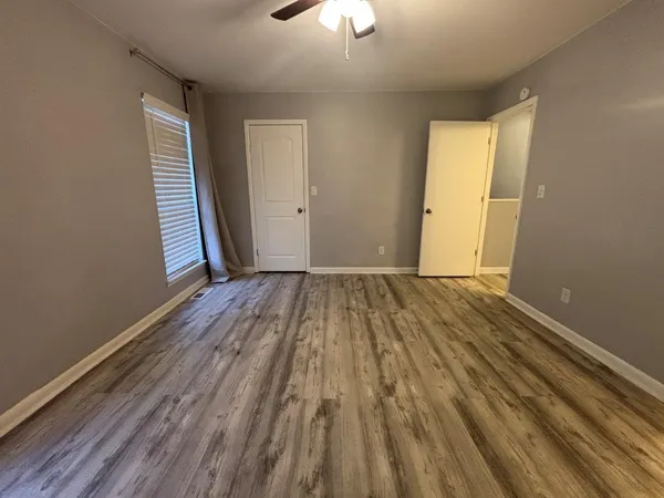 an empty room with wooden floor closet and windows