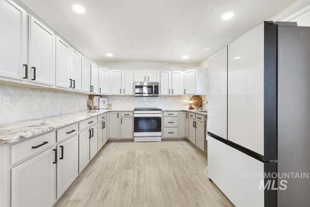 Kitchen with stainless steel appliances, light stone counters, light wood-type flooring, white cabinetry, and recessed lighting