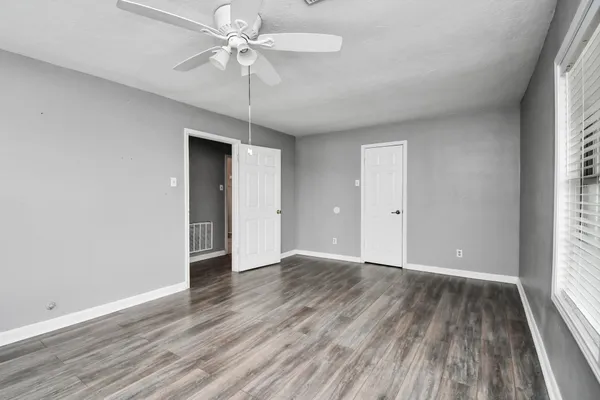 an empty room with wooden floor chandelier fan and windows