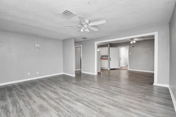 a view of an empty room with wooden floor and a ceiling fan