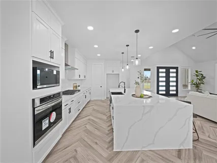 a large white kitchen with kitchen island a stove a sink a refrigerator and a dining table with wooden floor