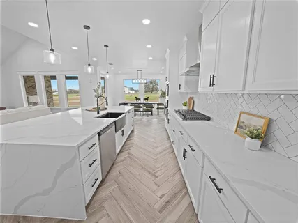 a large white kitchen with lots of counter space wooden floor and stainless steel appliances