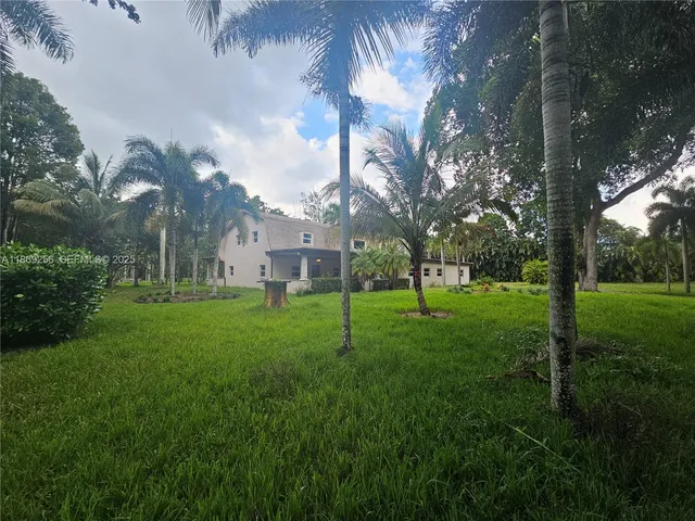 a view of a white house with a big yard and large trees