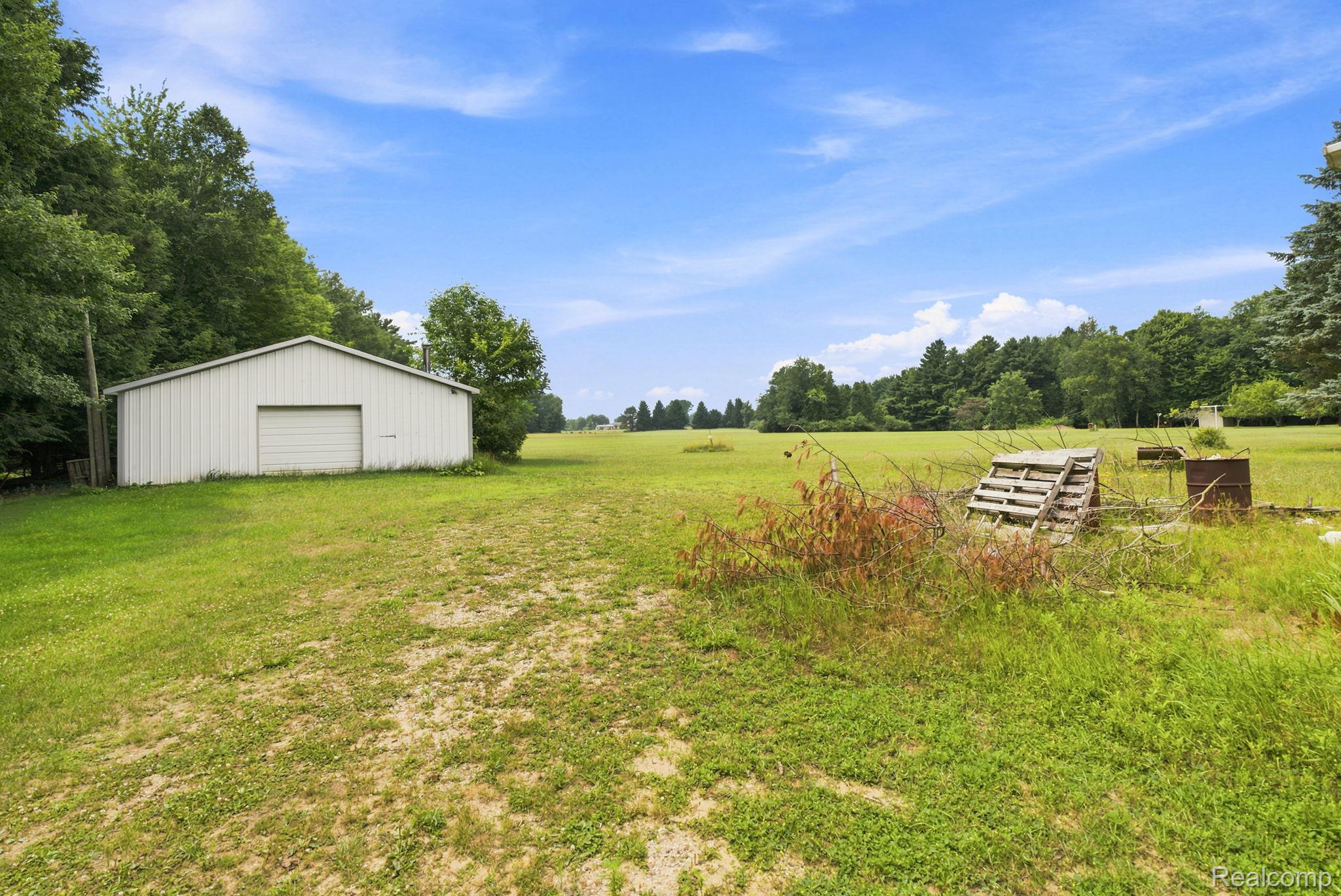 2390 Lakeshore Road Applegate, MI 48401 - Photo 32 of 97 Expansive pastoral setting featuring a level acreage with mature tree lines, a metal-frame storage structure, and rustic outbuildings ideal for agricultural or equestrian pursuits