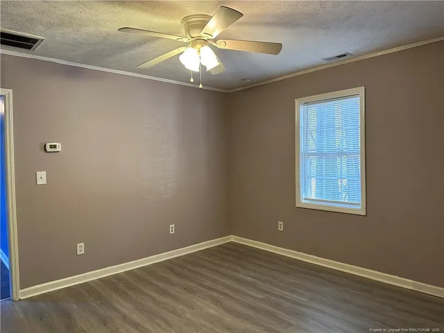 an empty room with wooden floor fan and windows