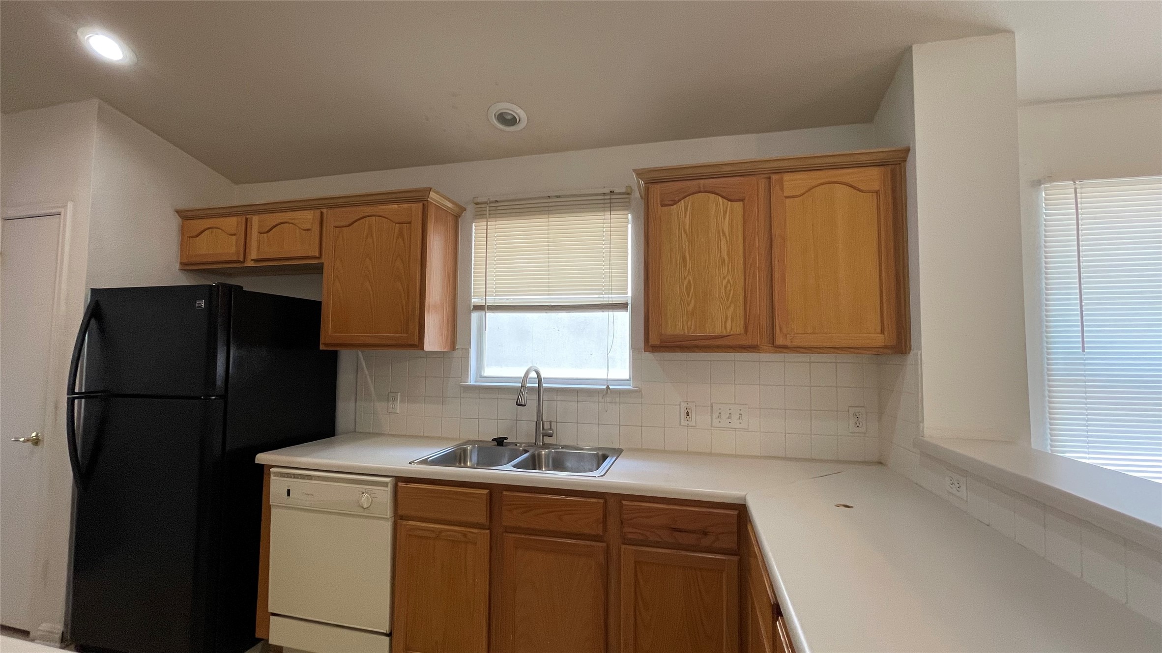 5512 Steven Creek Way Austin, TX 78721 - Photo 7 of 30 Kitchen featuring backsplash, light countertops, white dishwasher, brown cabinets, and freestanding refrigerator