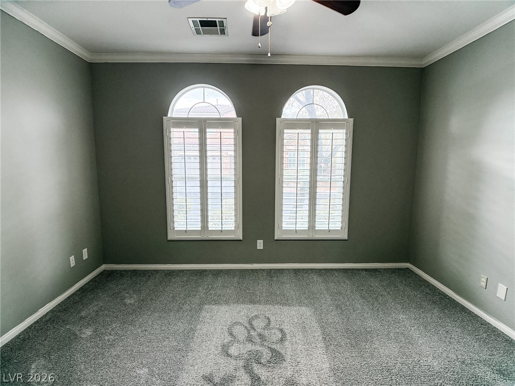 8683 Moreno Mountain Avenue Las Vegas, NV 89178 - Photo 12 of 26 Arch-topped windows illuminate this spacious room, featuring detailed crown molding and a patterned carpet.