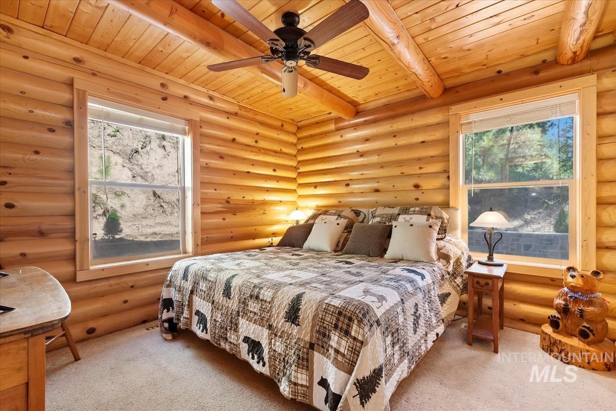 10 Elk Point Road Garden Valley, ID 83622 - Photo 21 of 42 Carpeted bedroom featuring log walls, multiple windows, a wooden ceiling with exposed beams, and a ceiling fan