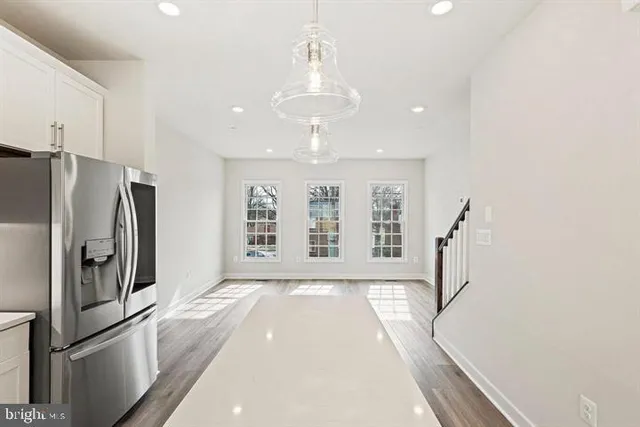a view of a refrigerator in kitchen and an empty room with wooden floor