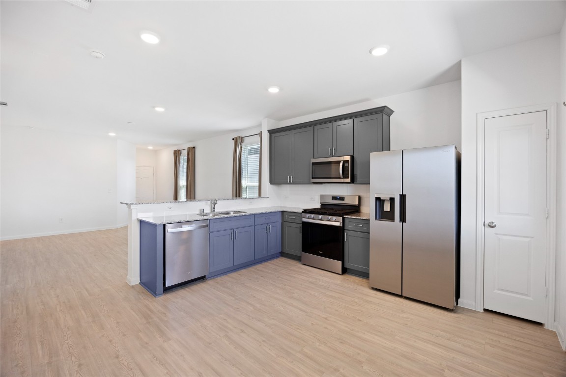 17907 Grain Auger Road Hockley, TX 77447 - Photo 12 of 24 modern kitchen with sleek stainless steel appliances, including a refrigerator, oven, and dishwasher. It features stylish gray cabinetry, a spacious countertop, and an open layout that flows into the living area with light wood flooring.