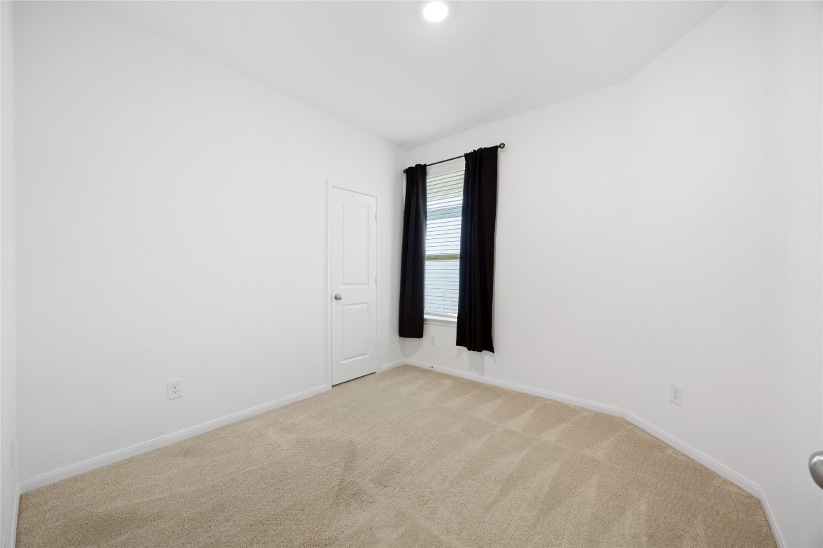 17907 Grain Auger Road Hockley, TX 77447 - Photo 15 of 24 small, bright room with clean white walls, beige carpet, and a window with black curtains. A closed door is on one wall, and a ceiling light illuminates the space.