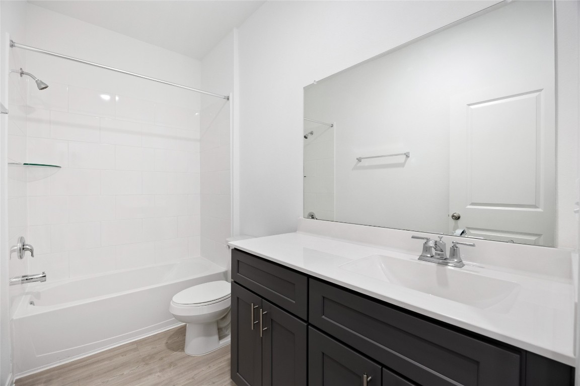 17907 Grain Auger Road Hockley, TX 77447 - Photo 16 of 24 modern bathroom with a clean design, featuring a white bathtub with a shower, dark cabinetry, and a large mirror above the sink. The space is bright and contemporary, with light wood flooring.