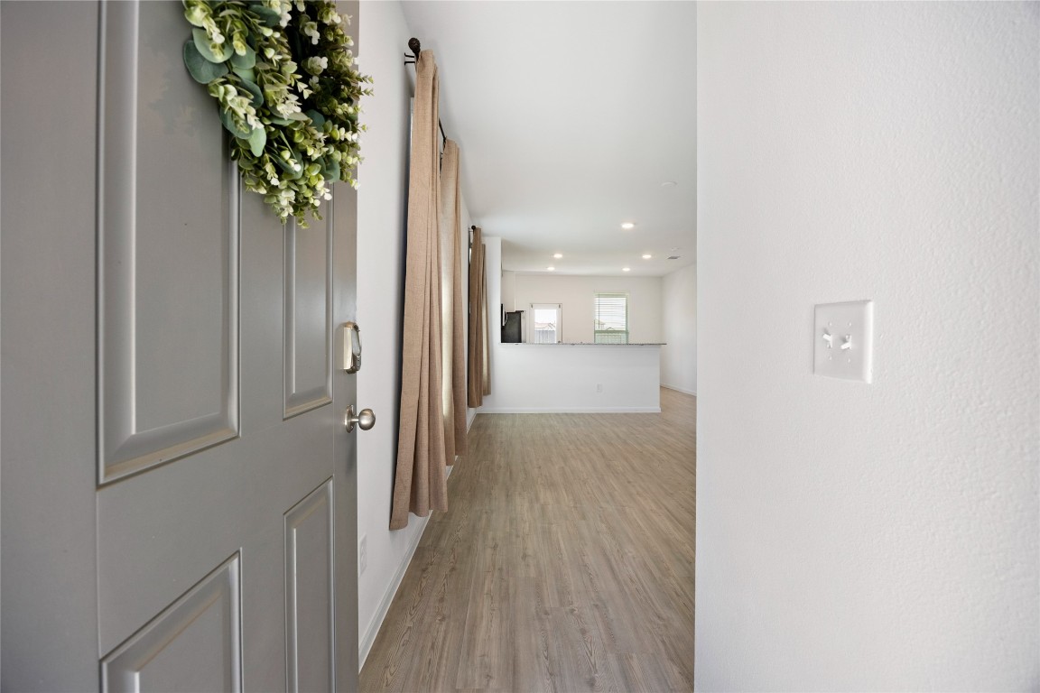17907 Grain Auger Road Hockley, TX 77447 - Photo 6 of 24 This photo shows a welcoming entryway with a light-colored door adorned with a wreath. It opens into a bright, open-concept living space featuring wood flooring, neutral walls, and modern lighting.