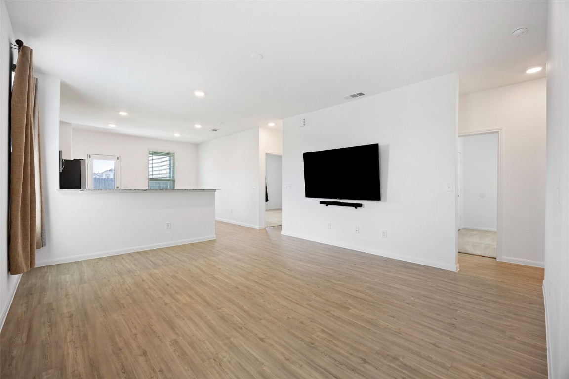 17907 Grain Auger Road Hockley, TX 77447 - Photo 7 of 24 Bright and spacious open-concept living area with wood-style flooring, a mounted TV, and an adjacent kitchen featuring a breakfast bar. Large windows provide ample natural light.