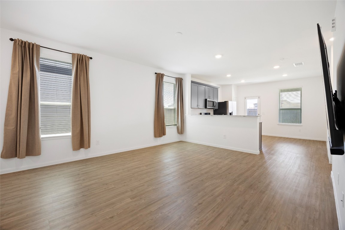 17907 Grain Auger Road Hockley, TX 77447 - Photo 8 of 24 spacious, open-concept living area with wood flooring and ample natural light. The kitchen features modern appliances and a breakfast bar, seamlessly connecting to the living space. Neutral tones and large windows enhance the room's airy feel.