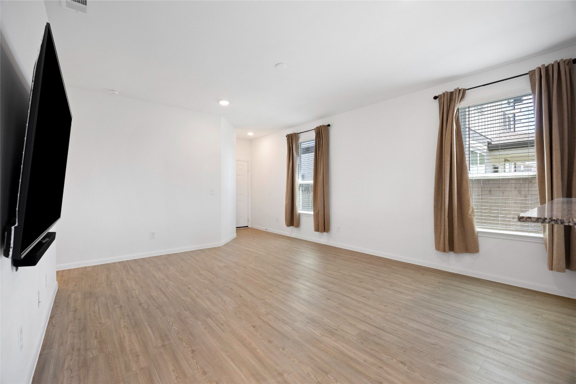 17907 Grain Auger Road Hockley, TX 77447 - Photo 9 of 24 Spacious living area with light wood flooring, large windows with brown curtains, and a wall-mounted TV, offering a bright and inviting atmosphere.