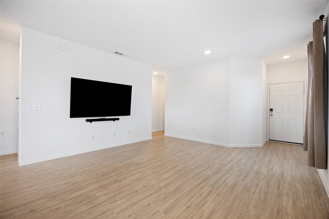 17907 Grain Auger Road Hockley, TX 77447 - Photo 10 of 24 Bright, open living space with light wood flooring, white walls, and a mounted TV. Recessed lighting adds modern touches, and a window with curtains brings in natural light. The entryway features a secure door with a keypad lock.