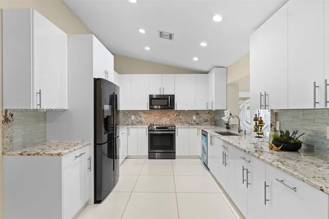 a large kitchen with stainless steel appliances granite countertop a stove top oven a sink and white cabinets