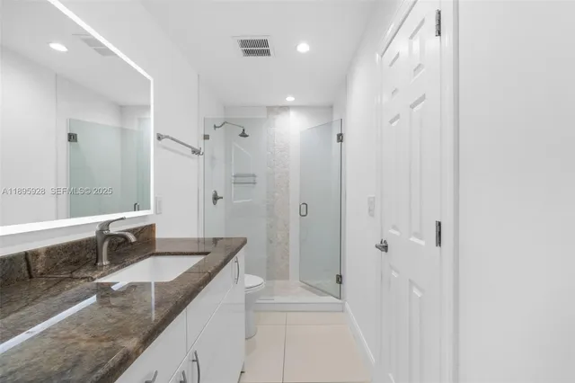 a bathroom with a granite countertop sink a toilet a large mirror and shower